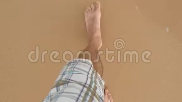 站在沙滩上踏着金沙的年轻人的观点雄腿在海洋附近行走光脚的家伙视频的预览图