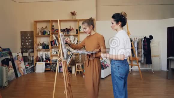瘦小的女美术学生正在画画正在和她友好的老师谈话视频的预览图
