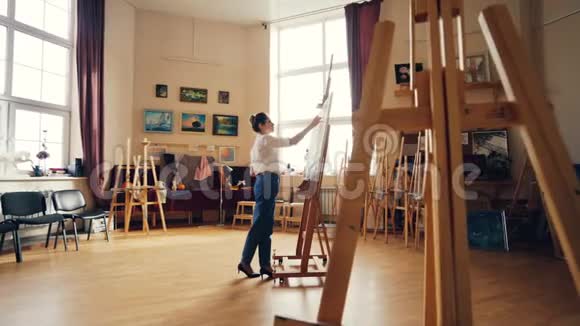 年轻的女画家正在室内画画独自在灯光车间里工作木制画架正宗艺术品视频的预览图