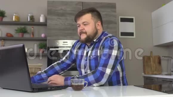 一个留着胡子的男人坐在厨房里一边喝着咖啡一边失望地看着笔记本电脑一边输视频的预览图