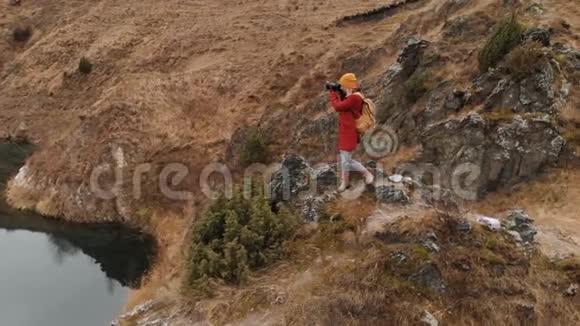 一个女孩站在湖岸的岩石上在她的单反相机上拍摄风景视频的预览图