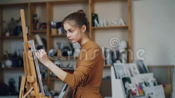 美丽的金发画家是在艺术工作室单独使用画眉和调色板与油漆年轻女子视频的预览图
