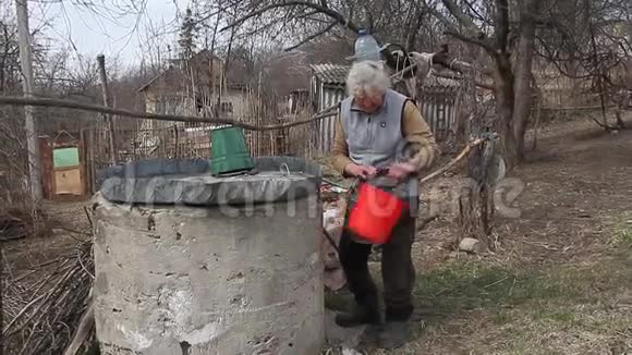 一个荒无人烟的村庄里的一个老妇人正从一个桶里的井里取水独自生活视频的预览图