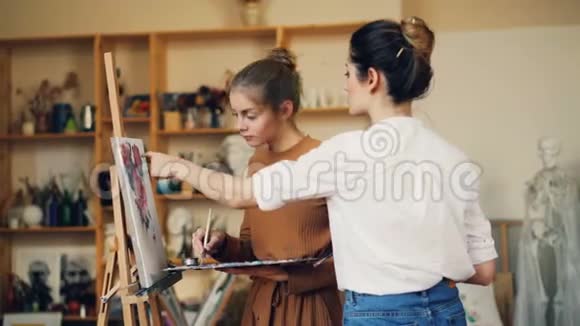 美丽的年轻女画家正在教她的学生画在画室里工作的花和油画视频的预览图