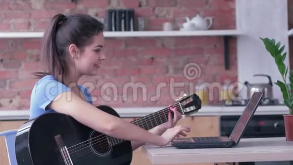 有魅力的吉他手女子学习演奏弦乐器使用笔记本电脑在线视频教学和视频的预览图