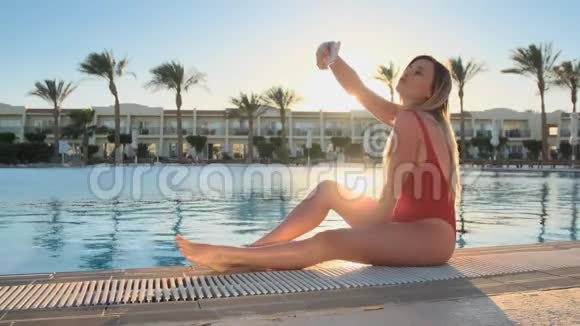 玩得开心的女孩在游泳池附近用手机拍照穿红色时髦比基尼泳装的性感女人做自拍视频的预览图