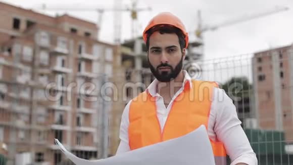 施工工人戴橙色头盔看镜头的肖像有建筑工程的建筑工人站起来视频的预览图