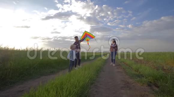 快乐的童年手里拿着风筝的孩子在户外娱乐的时候在乡下的父母身边奔跑视频的预览图