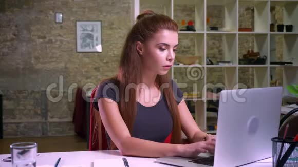 疲惫的白种人女孩抱着她的头一边看着笔记本电脑一边挣扎一边坐在办公室的录像里视频的预览图