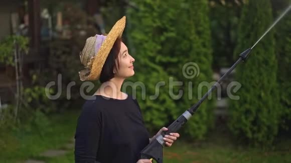 微笑的亚洲女人戴着草帽用软管浇树视频的预览图