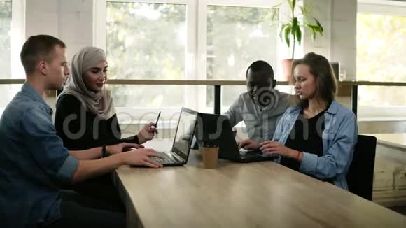 不同的人使用笔记本电脑而坐在窗前明亮的工作场所多种族和多文化视频的预览图
