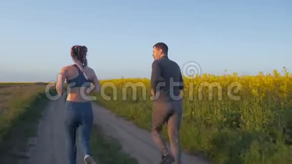 户外运动年轻的运动员和戴着卡尼卡隆辫子的女性在蓝色的油菜花草坪上在大自然中奔跑视频的预览图