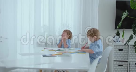 两个男孩兄弟坐在客厅的一张桌子旁用铅笔在纸上画画妈妈过来拥抱孩子们视频的预览图