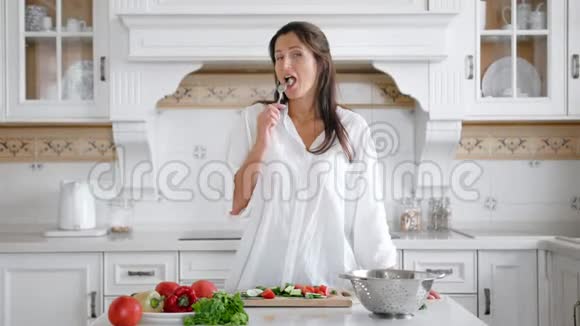 微笑着穿着白色衬衫的年轻女人一边吃纯素沙拉一边品尝新鲜的有机黄瓜片视频的预览图