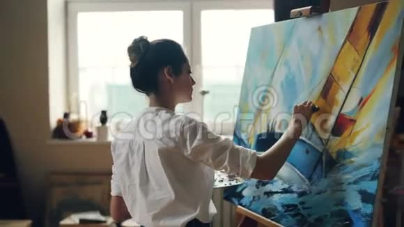 严肃的女艺术家用油画和调色刀在画中描绘美丽的海洋景观视频的预览图