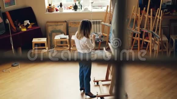 有创造力的年轻女士忙于绘画独自在现代工作室工作配备木制家具画架和艺术工具视频的预览图