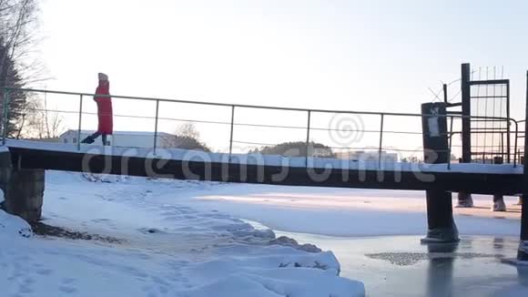 穿着红色长夹克的年轻女子走在冰雪覆盖的码头上站在冰冻的河岸上视频的预览图