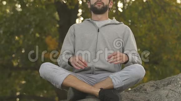 活泼的男人坐在岩石顶部的莲花位置冥想和放松爱好视频的预览图