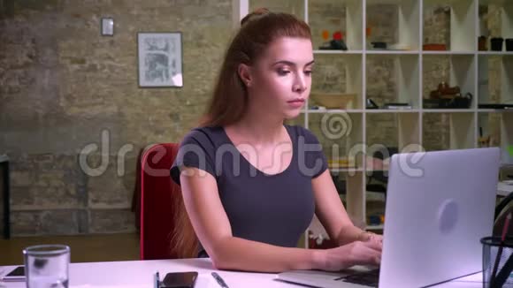 一个严肃的女人正坐在手机上一边看着她的笔记本电脑屏幕说话视频的预览图
