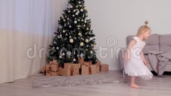 小可爱的女孩穿着白色连衣裙在家中的圣诞树附近跳舞视频的预览图