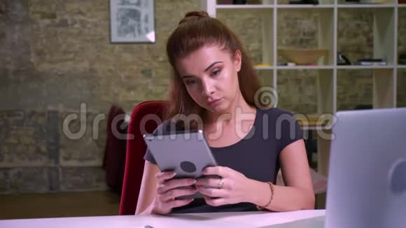 红发美丽的白种人女性的一张无聊的脸她坐在办公室里平静地淡淡地看着她的平板电脑视频的预览图