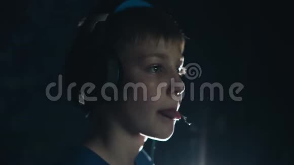 一个头戴耳机的男孩在黑暗的房间里玩电子游戏脸上的情绪视频的预览图