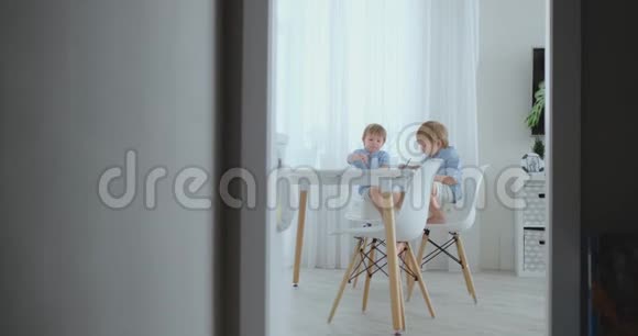 两个男孩兄弟坐在客厅的一张桌子旁用铅笔在纸上画画妈妈过来拥抱孩子们视频的预览图