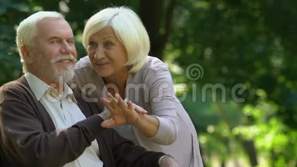 一对老夫妇拥抱在一起高兴地看着他们的孙子们在公园玩耍视频的预览图
