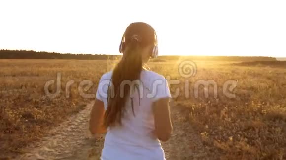 美丽的女孩在乡村日落时做体育锻炼戴着耳机的女孩沿着路跑听着视频的预览图