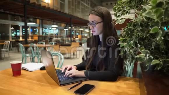 戴眼镜的年轻女孩在木桌上用笔记本电脑工作视频的预览图