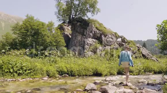 女人过河去石头旅游妇女踩在流动的河流上的石头上视频的预览图