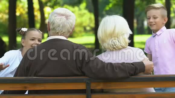 小男孩和小女孩来到祖父母坐在公园的长凳上家庭日视频的预览图