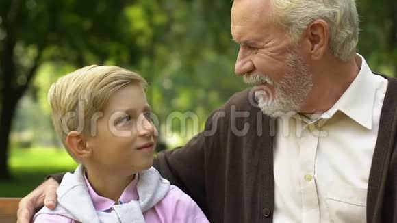 笑着爷爷和孙子坐在公园的长凳上竖起大拇指签名视频的预览图
