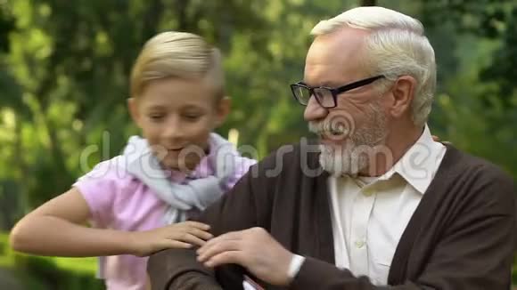 小可爱的男孩坐在爷爷旁边的长凳上给他看家庭相册视频的预览图