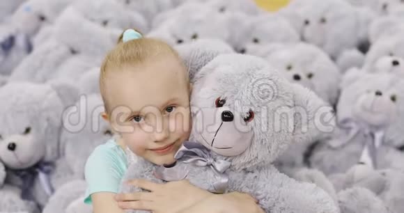 一个可爱的女孩抱着一只柔软的熊背景是一堆玩具视频的预览图