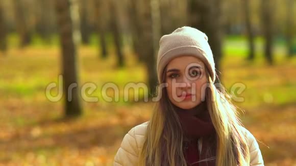 一个美丽的女孩在秋天公园里看着相机摘下帽子悲伤开始大笑视频的预览图