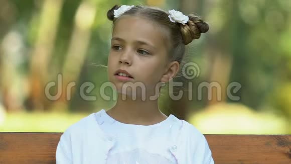 困惑的小女孩独自坐在长凳上环顾四周缺乏朋友视频的预览图