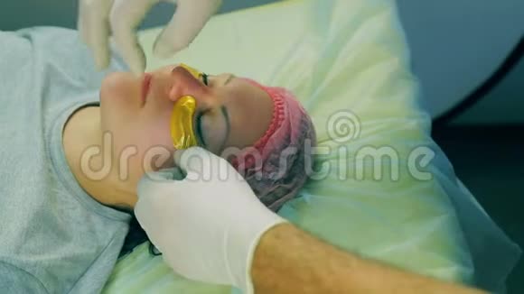 戴着手套的男性美容师的双手将胶原蛋白垫在眼睛下面贴在女人脸上视频的预览图