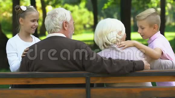 小可爱的孩子们和坐在公园长凳上的爷爷奶奶愉快地交谈着视频的预览图