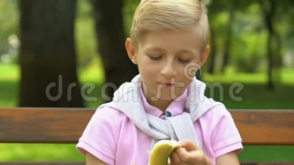 小男孩坐在长凳上课间吃香蕉吃健康零食视频的预览图