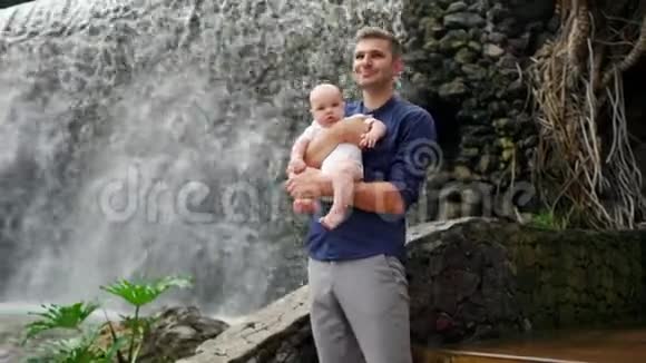 家庭自然之旅父亲和一个小女孩在夏天的雨天森林里看瀑布视频的预览图