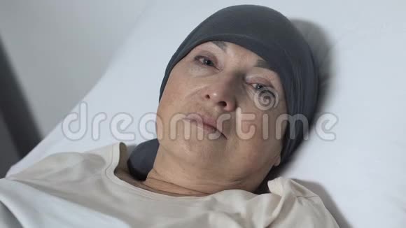 让戴着围巾躺在床上看着摄像机的老太太心烦意乱化疗病人视频的预览图