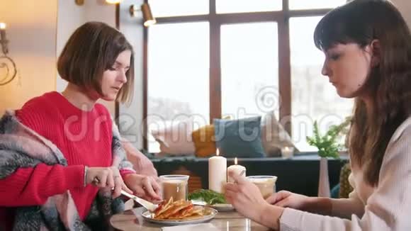 两个年轻的女人坐在咖啡馆里边吃煎饼边说话伟大的现代内部视频的预览图