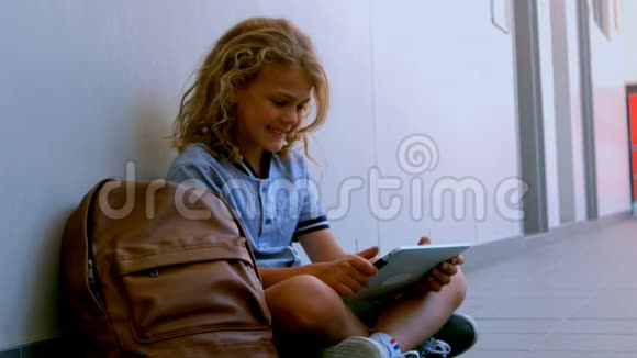 可爱的高加索女学生坐在地板上在学校走廊里使用数字平板电脑视频的预览图