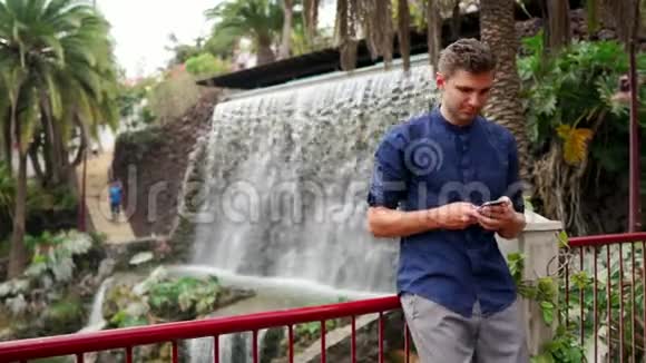 帅气的年轻商人户外滑动智能手机触摸屏瀑布视频的预览图