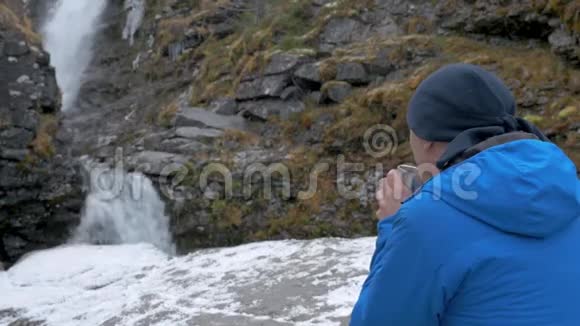 一个穿着运动服的人在瀑布前休息他喝杯子里的茶视频的预览图