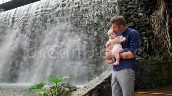 父亲带着孩子微笑拥抱婴儿的儿子关于瀑布亲吻和交谈幸福的概念视频的预览图