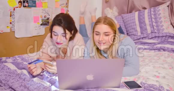 两个女孩用笔记本电脑在线购物漂亮的青少年在互联网上购买商品粉色背景卧室视频的预览图