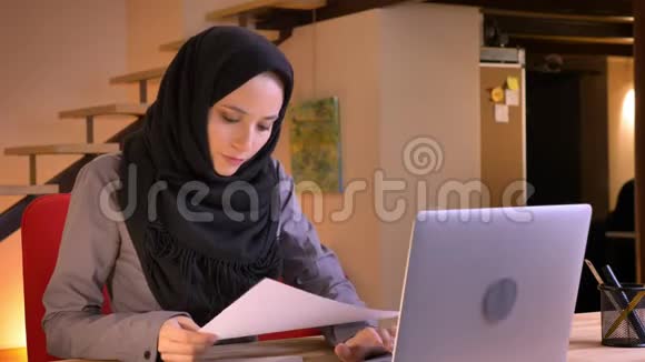年轻的穆斯林女商人在笔记本电脑上打字然后看着相机微笑的特写照片视频的预览图