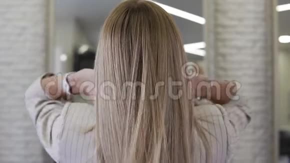 漂亮的金发女人慢慢地把她长长的波浪状的头发扔到室内视频的预览图